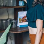 Sustainable Marketing - Woman Picking Up a Cup on Brown Wooden Shelf