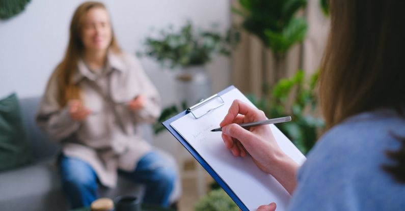 Work-life Help - Unrecognizable professional female psychologist writing on clipboard while sitting against client on blurred background during psychotherapy session in light office