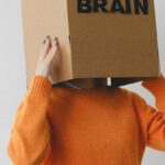Reconnecting Purpose - Crop person putting Idea title in cardboard box with Brain inscription on head of female on light background