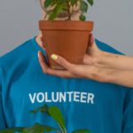 Volunteering Growth - Person in Blue Crew Neck T-shirt Holding Brown Potted Green Plants