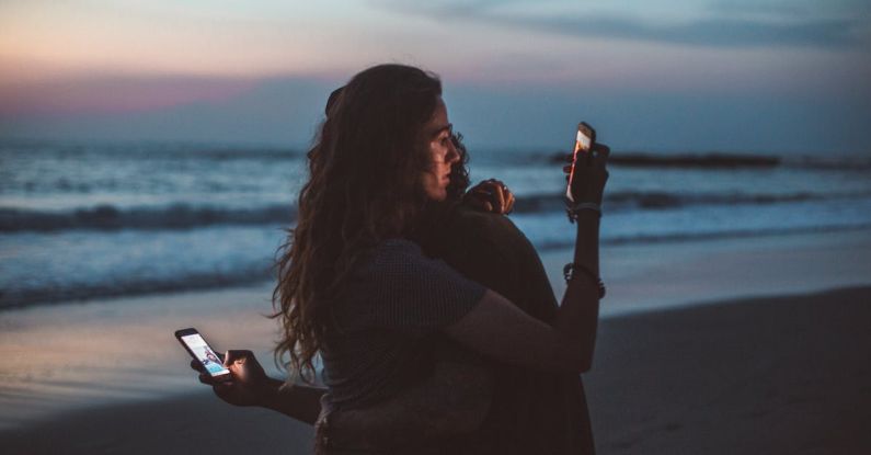 Managing Screentime - Couple hugging and using smartphone near sea on sunset