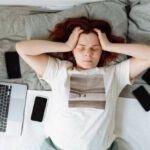 Digital Burnout - A Stressed Woman Lying on a Bed beside Cellphones and a Laptop