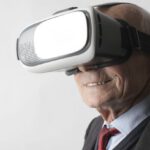 Virtual Reality Wellbeing - Smiling elderly gentleman wearing classy suit experiencing virtual reality while using modern headset on white background