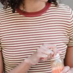 Digital Detox Retreats - Happy young ethnic female student with curly hair in trendy outfit smiling and looking away while drinking fresh juice sitting on stairs on street with modern laptop on knees