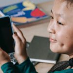 Educating Children Digital - Joyful ethnic child using mobile phone at school
