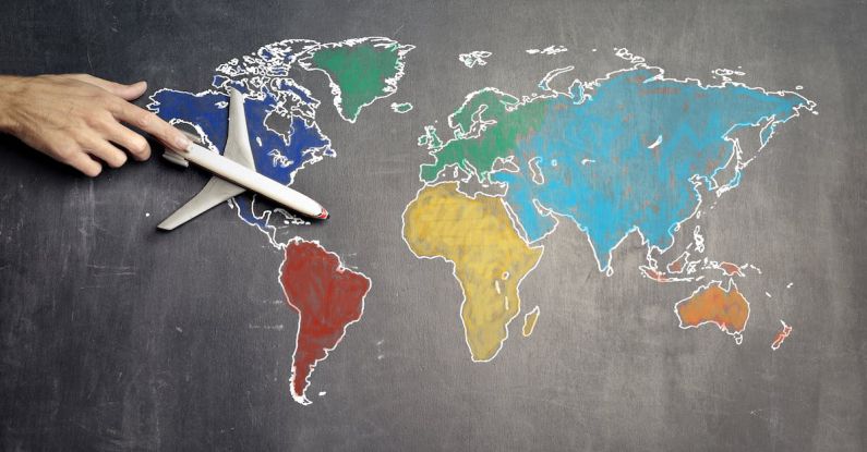 Impact Strategy - Top view of crop anonymous person holding toy airplane on colorful world map drawn on chalkboard