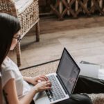 Accelerator Program - Young barefoot woman using laptop on floor near books in stylish living room